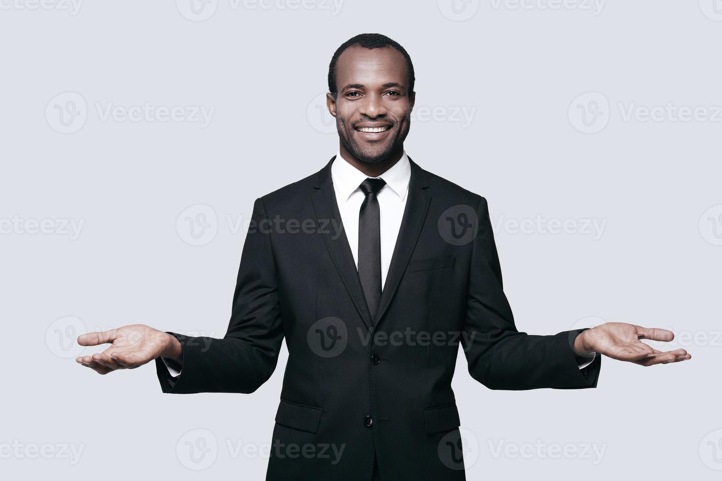 Open to new deals. Handsome young African man in formalwear gesturing and looking at camera while standing against grey background photo