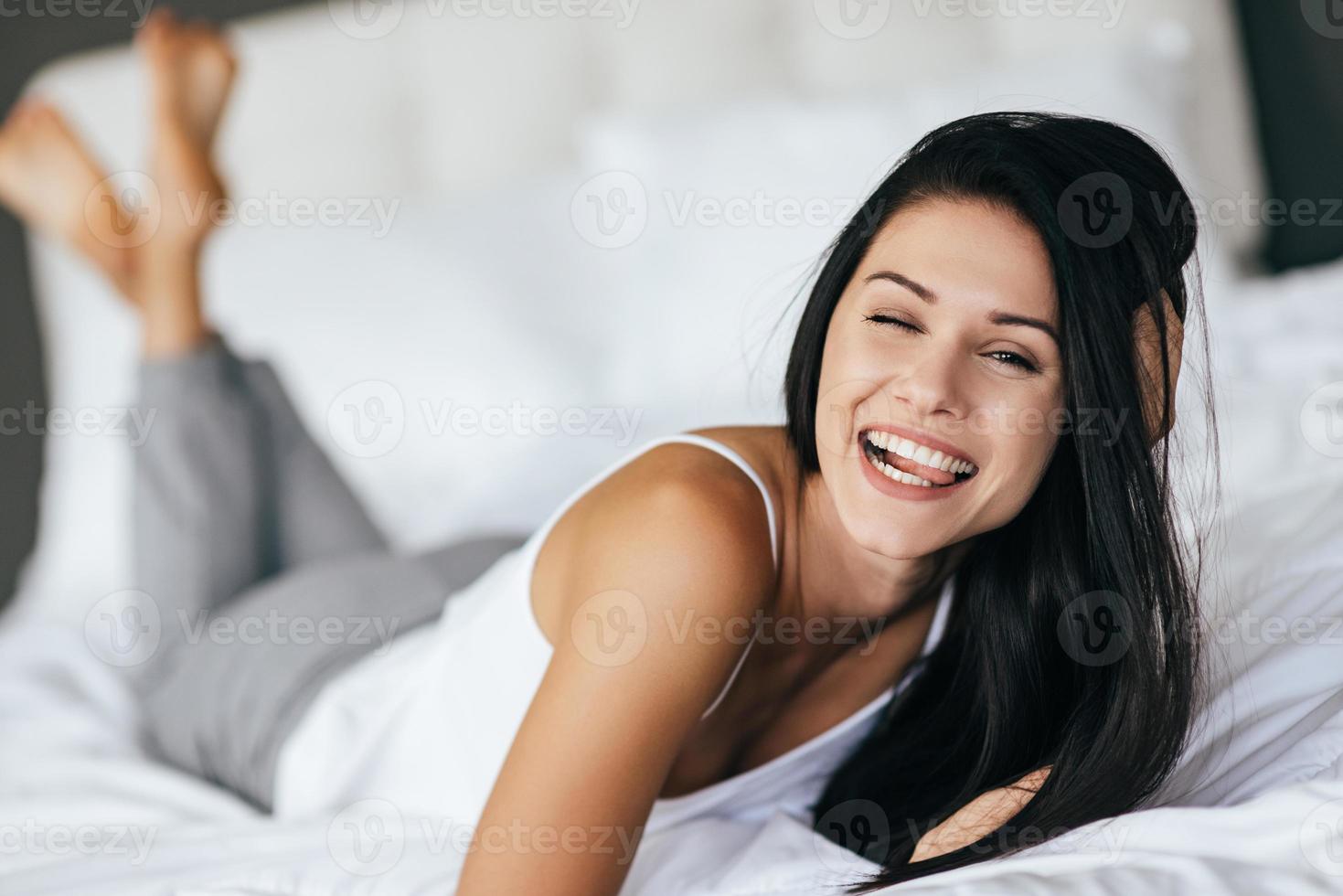 Making a face. Young woman making a face and smiling while lying on the bed at home photo