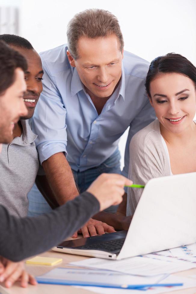 lluvia de ideas del equipo creativo. grupo de empresarios con ropa informal sentados juntos en la mesa y discutiendo algo mientras miran la laptop foto