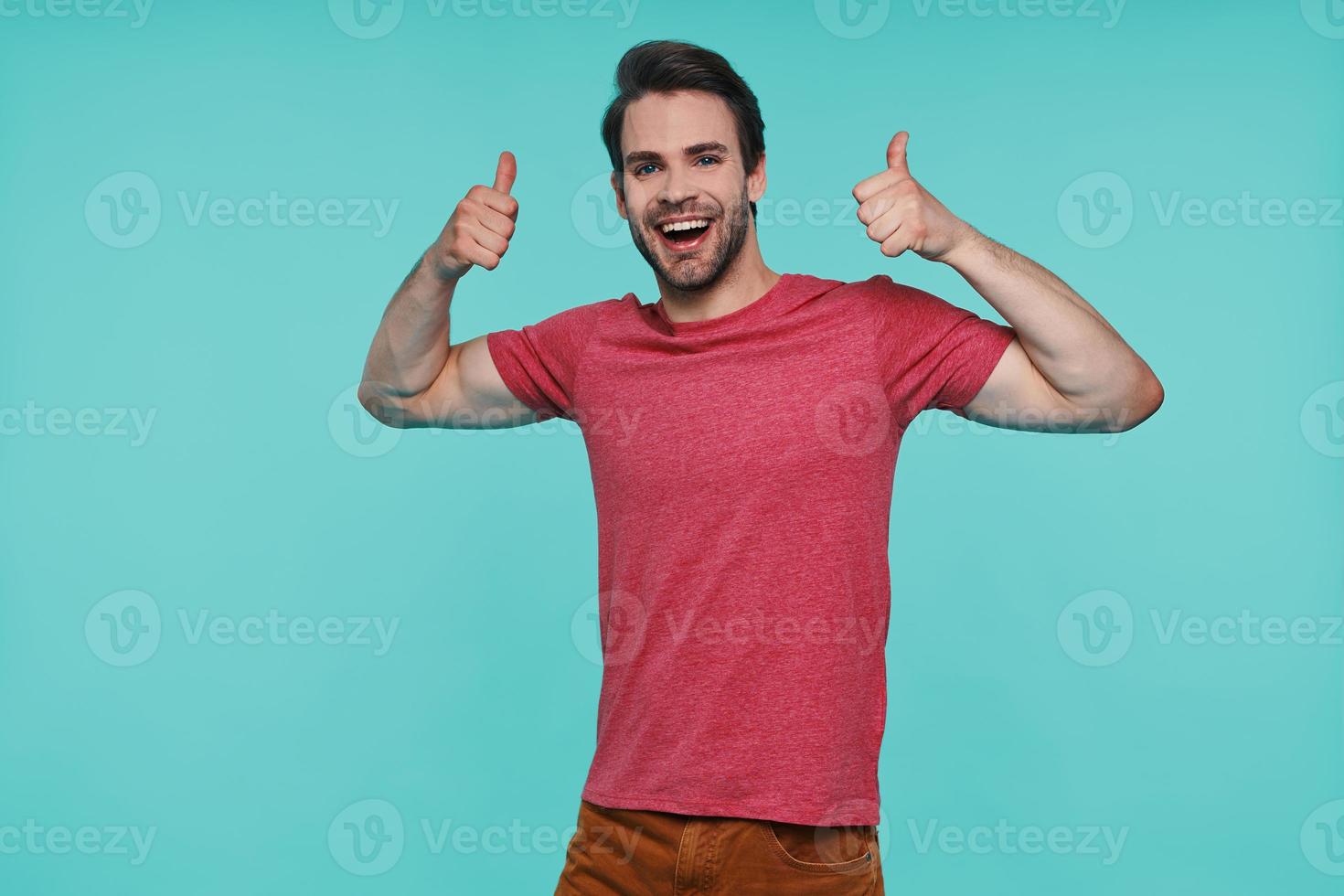 Handsome young smiling man in casual clothing looking at camera and showing his thumbs up photo