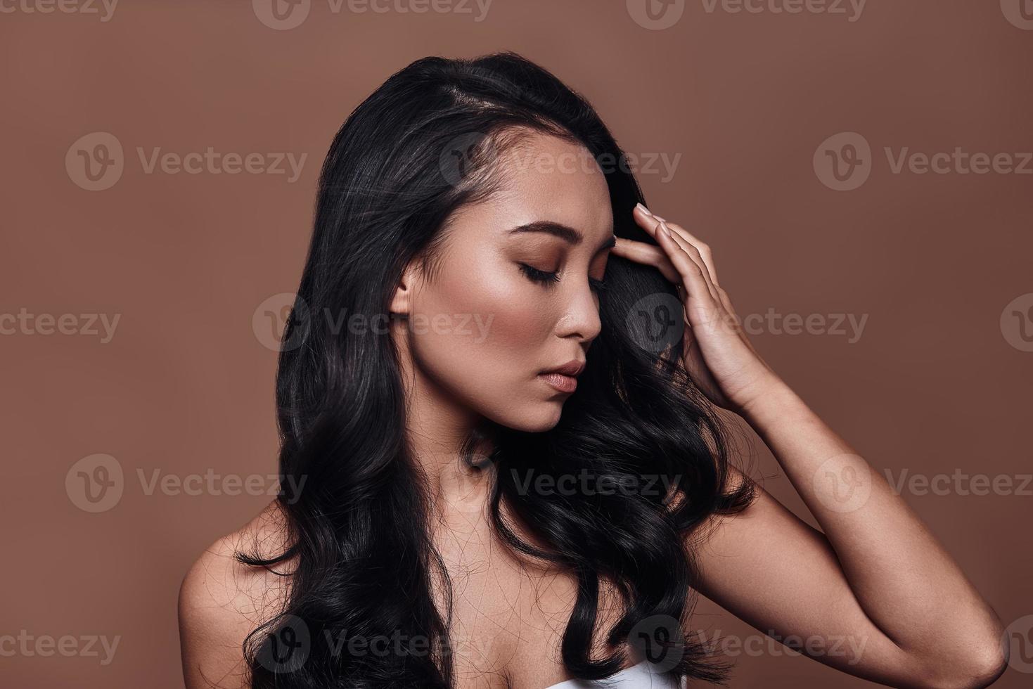 Perfect beauty. Beautiful young woman keeping eyes closed while standing against brown background photo