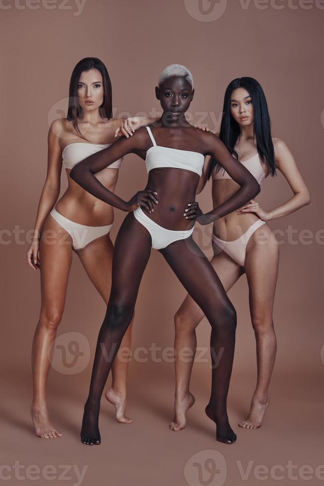 Born to be beautiful. Full length of three attractive mixed race women looking at camera while standing against brown background photo