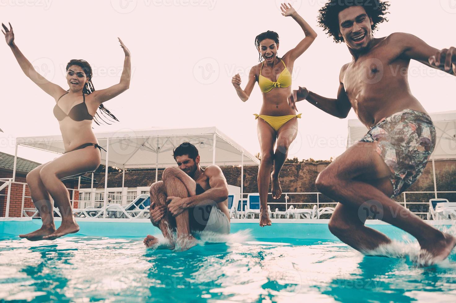 fiesta de piscina. grupo de hermosos jóvenes que se ven felices mientras saltan juntos a la piscina foto