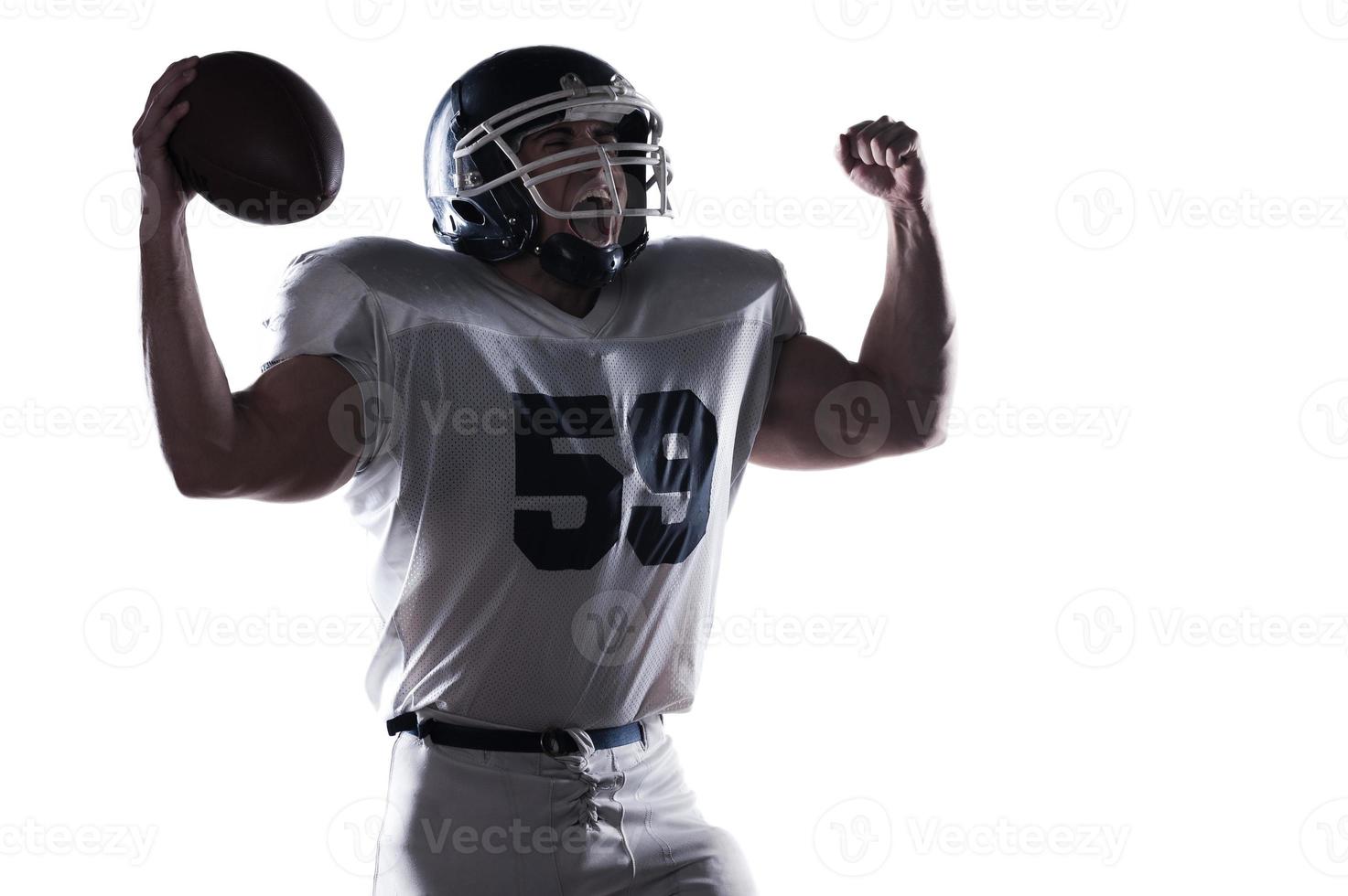 Emotions going wild.  American football player screaming and keeping arms raised while standing against white background photo