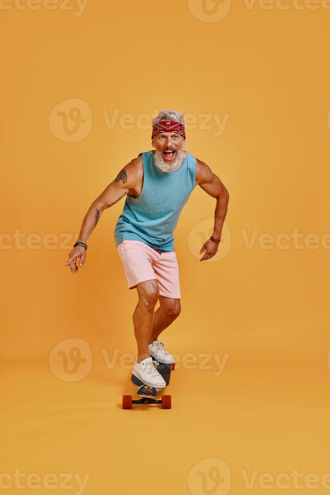 Full length of active senior man skateboarding against orange background photo