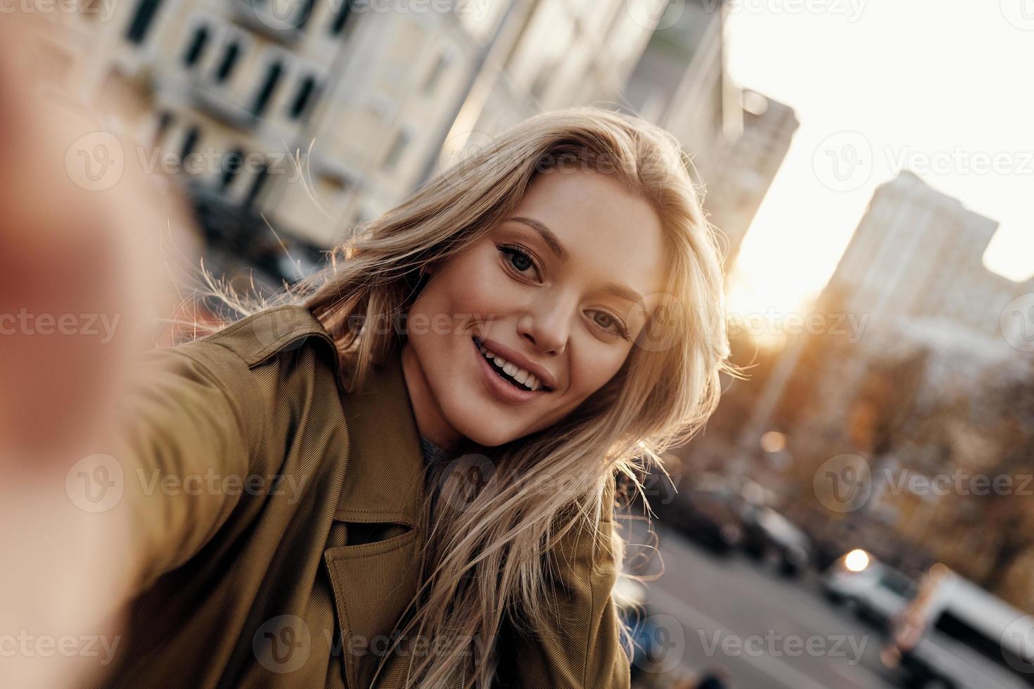 hermosa belleza autorretrato de una joven atractiva mirando a la cámara y sonriendo mientras está de pie al aire libre foto