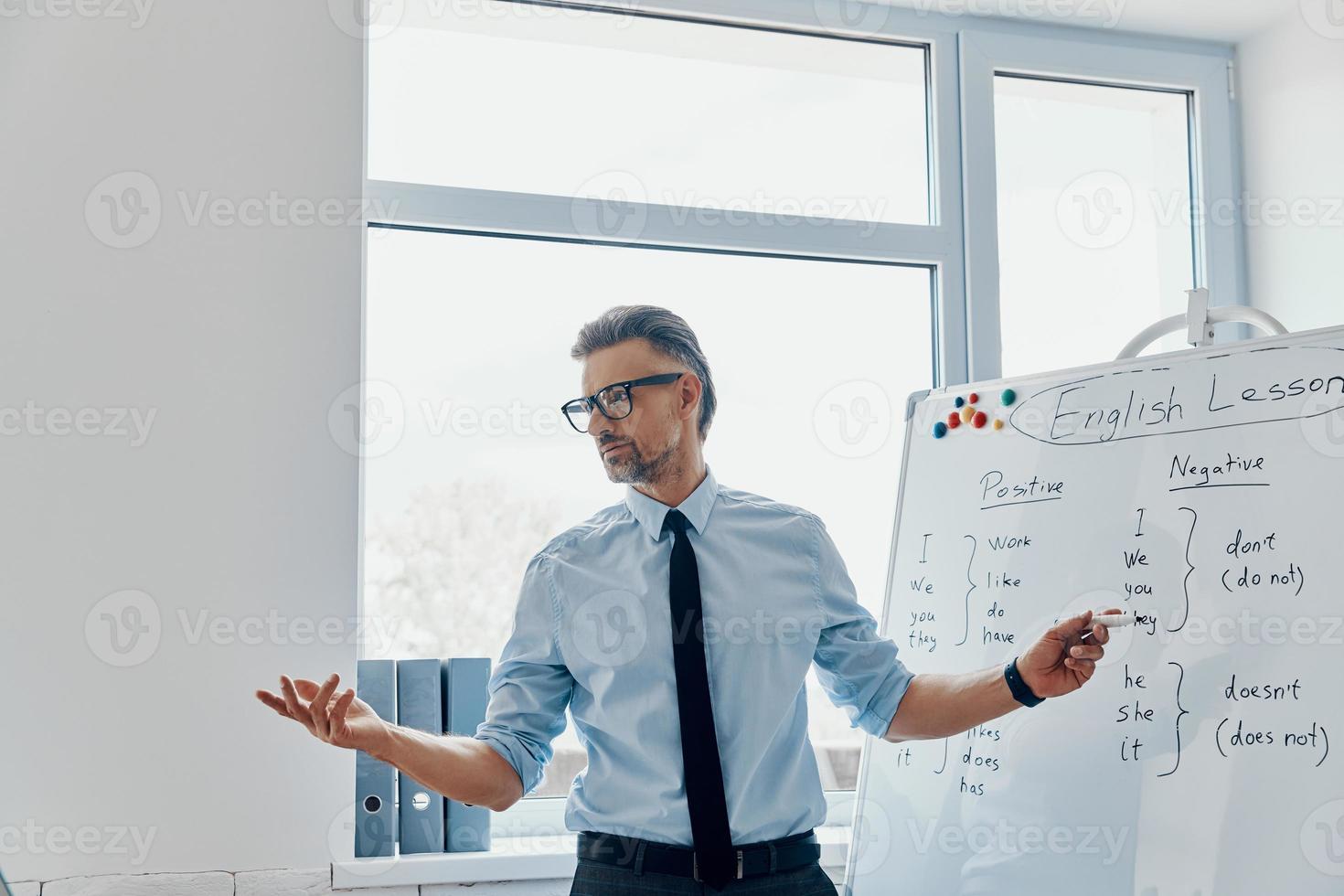Confident English teacher pointing whiteboard while standing at the classroom photo