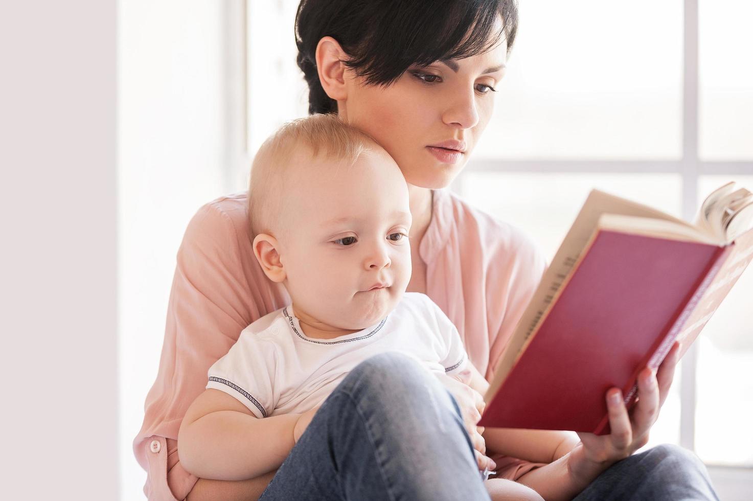 Reading a book together. Young mother holding baby and reading a book photo