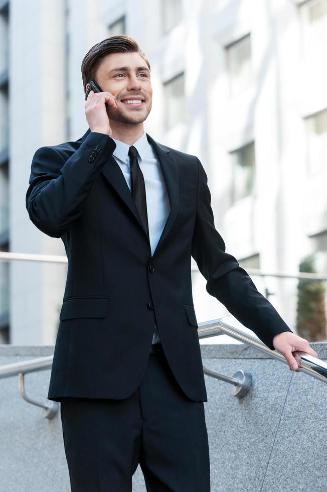 Successful businessman. Cheerful young men in formalwear talking on the mobile phone while going downstairs photo