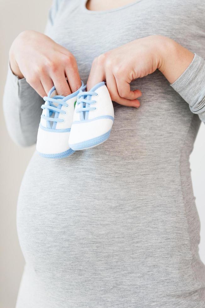 Expectation. Cropped image of pregnant woman holding little baby booties near her abdomen photo