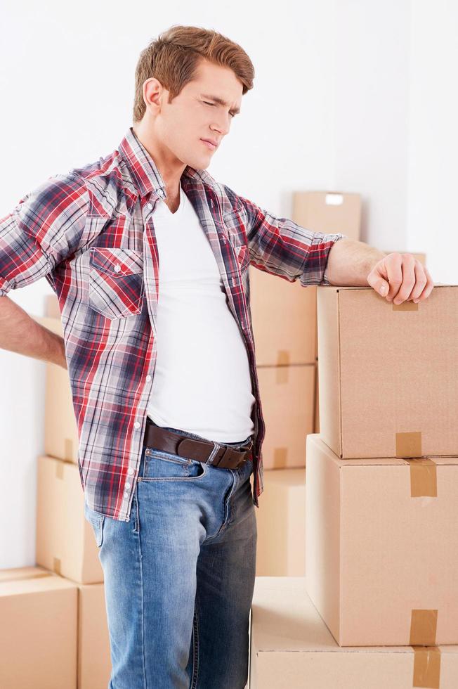 Feeling pain in back. Young man holding hand on his back and expressing negativity while leaning at the cardboard box photo