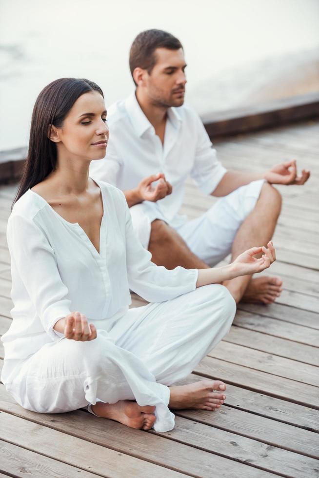 Mediating together. Top view of beautiful young couple in white clothing meditating outdoors together and keeping eyes closed photo