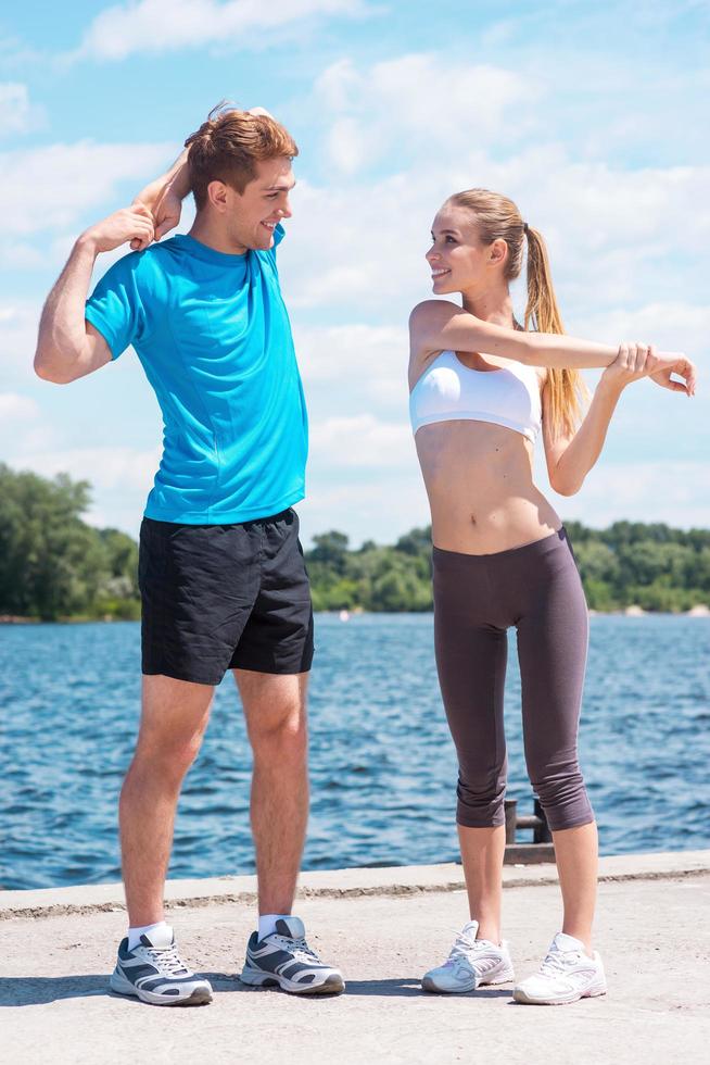 hacer ejercicio juntos es divertido. hermosa mujer joven y hombre haciendo ejercicios de estiramiento juntos mientras están de pie al aire libre foto