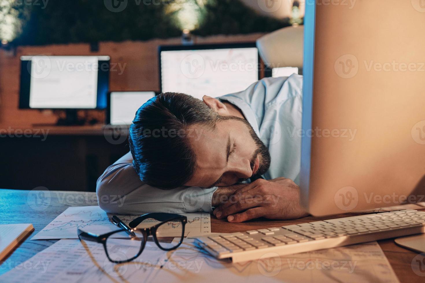 Exhausted young man sleeping at his working place while staying late in the office photo