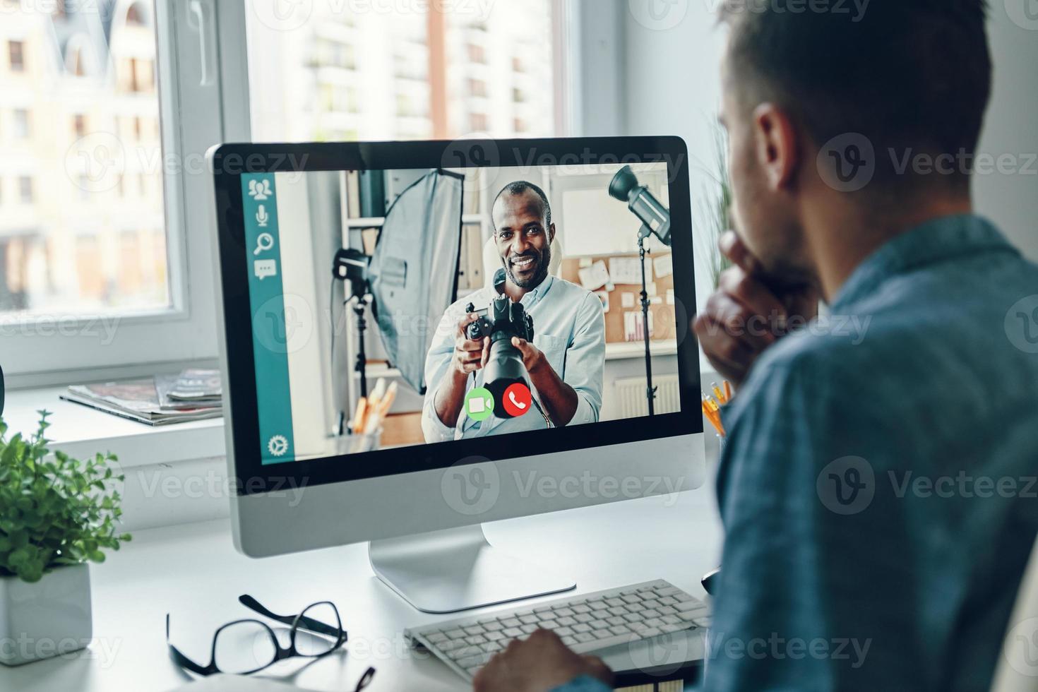 Confident young man talking to collegue by video call while sitting in office photo