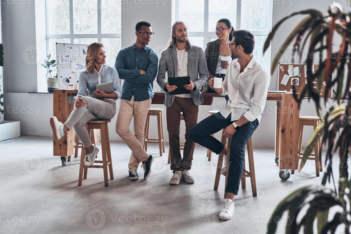 Young and successful team. Full length of young modern people in smart casual wear smiling and discussing something while working in the creative office photo