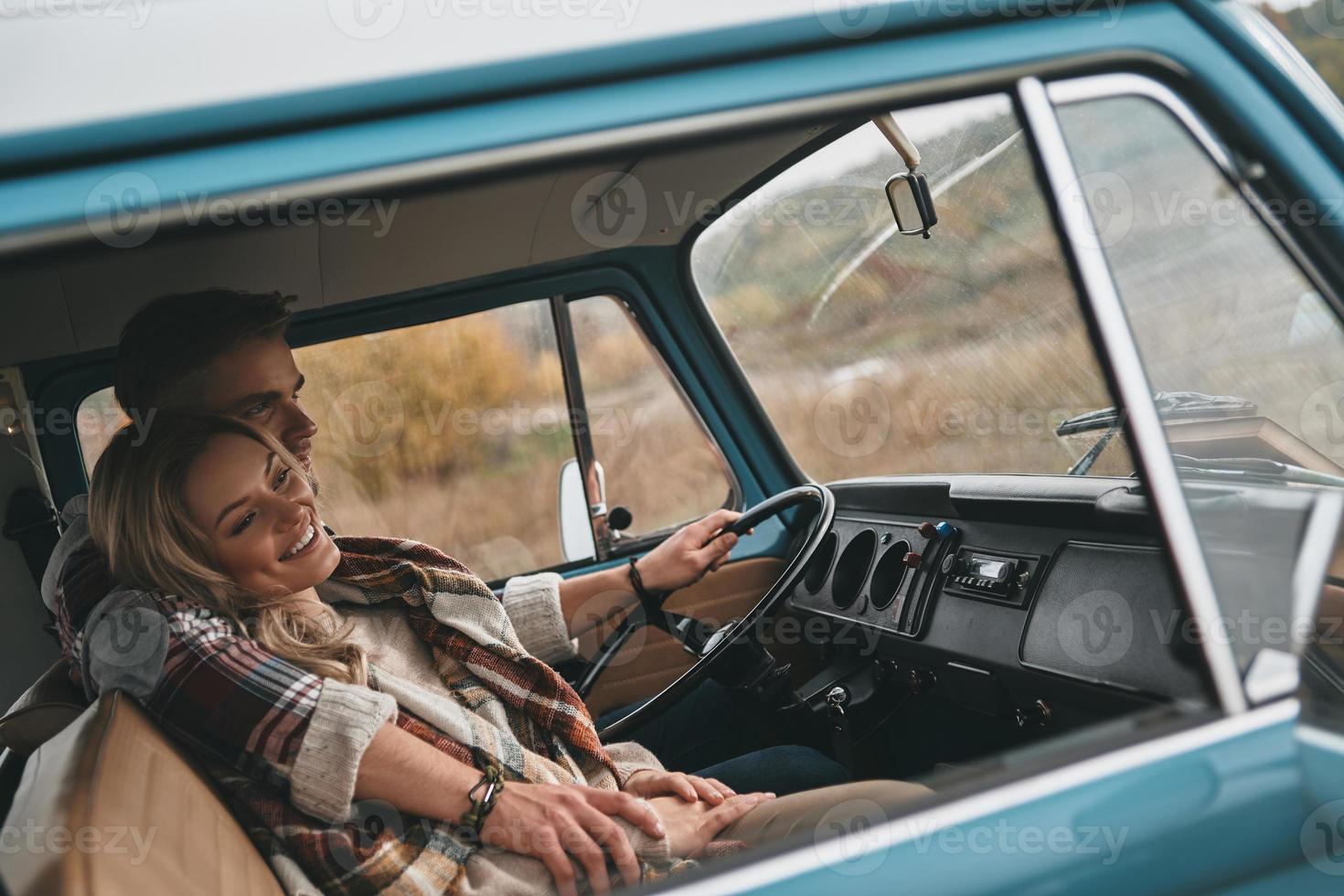 Totally happy. Beautiful young couple embracing and smiling while sitting in blue retro style mini van photo