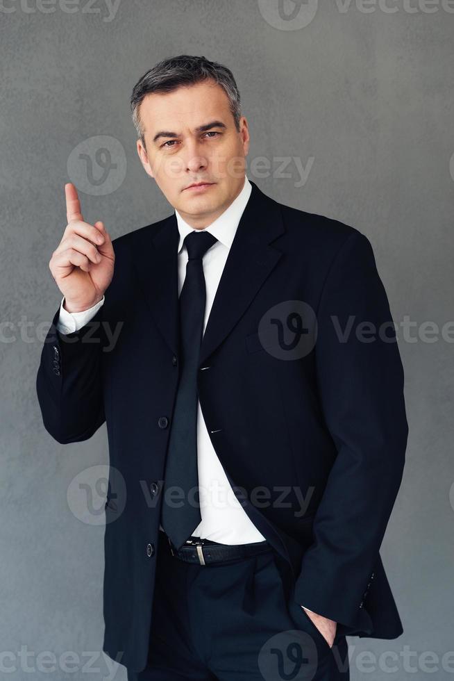 Great business idea. Mature businessman gesturing and looking at camera while standing against grey background photo