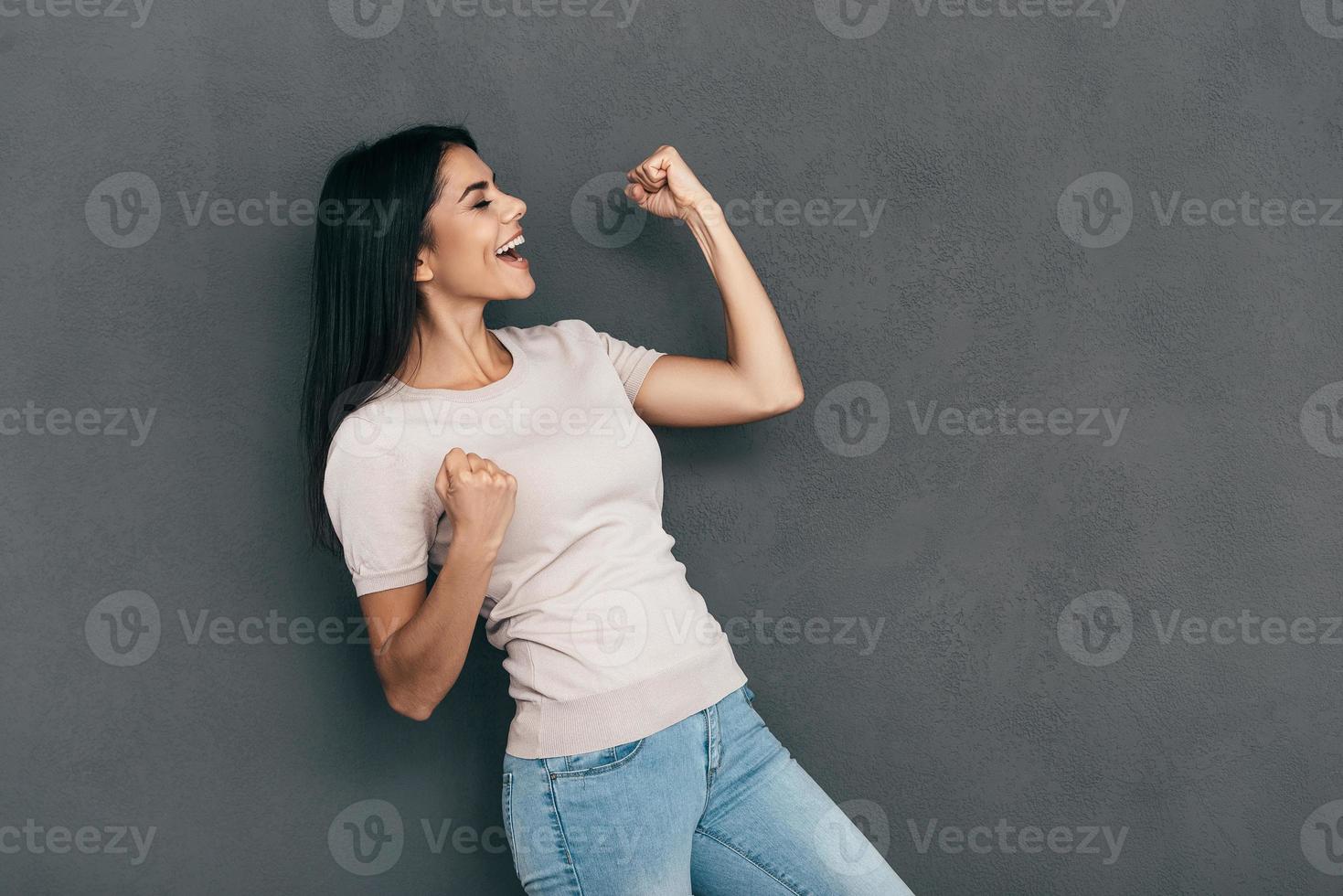 acostumbrado al éxito. mujer joven feliz en ropa casual gesticulando y manteniendo los ojos cerrados mientras está de pie contra el fondo gris foto