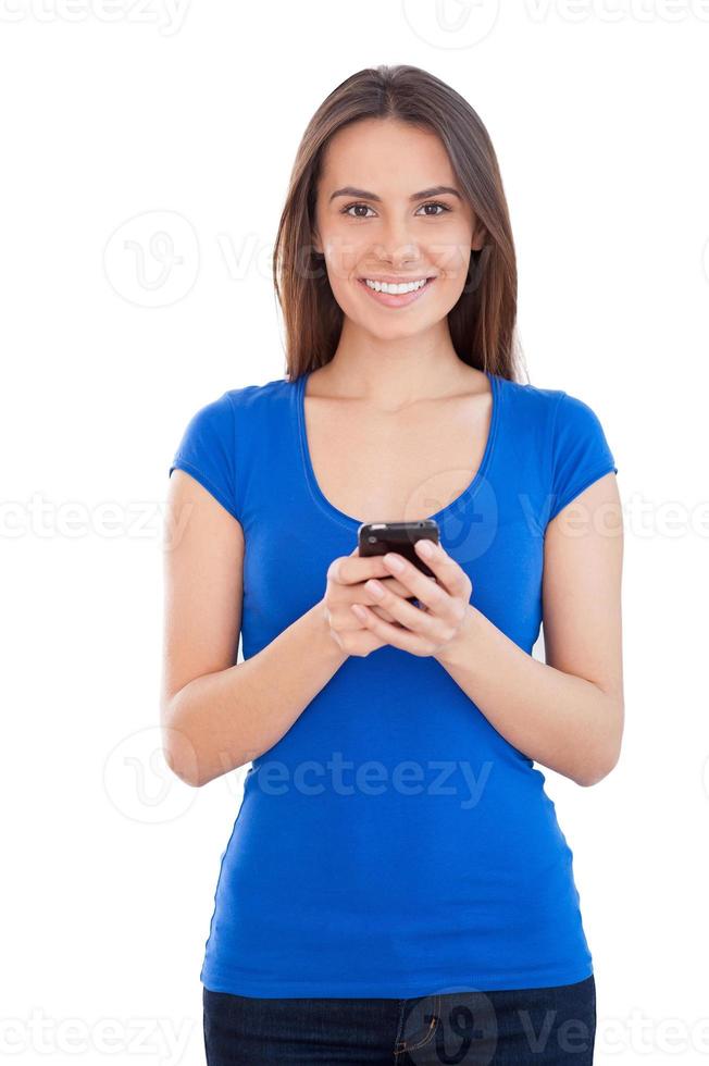 Beauty with mobile phone. Cheerful young woman holding mobile phone and smiling while standing isolated on white photo