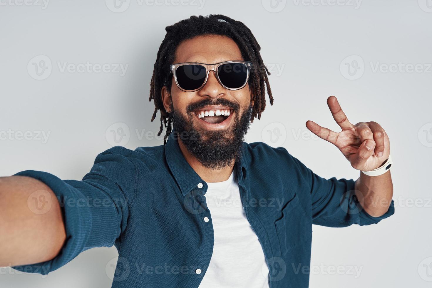 autorretrato de un joven africano con estilo mirando la cámara y sonriendo mientras se enfrenta a un fondo gris foto