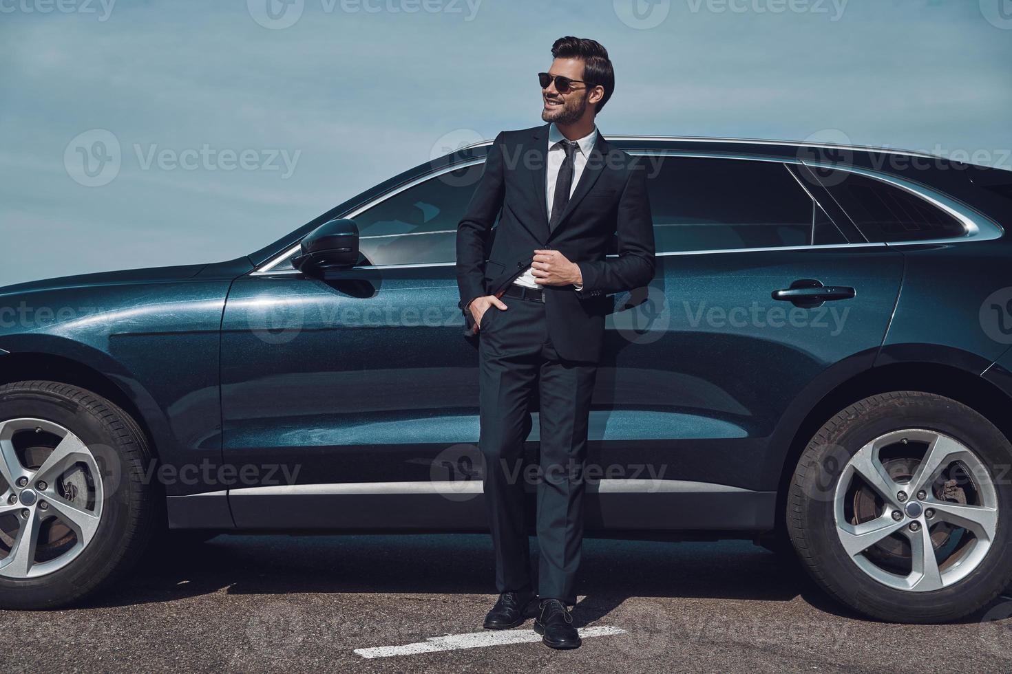 Great sense of style. Full length of handsome young businessman smiling while standing near his car outdoors photo