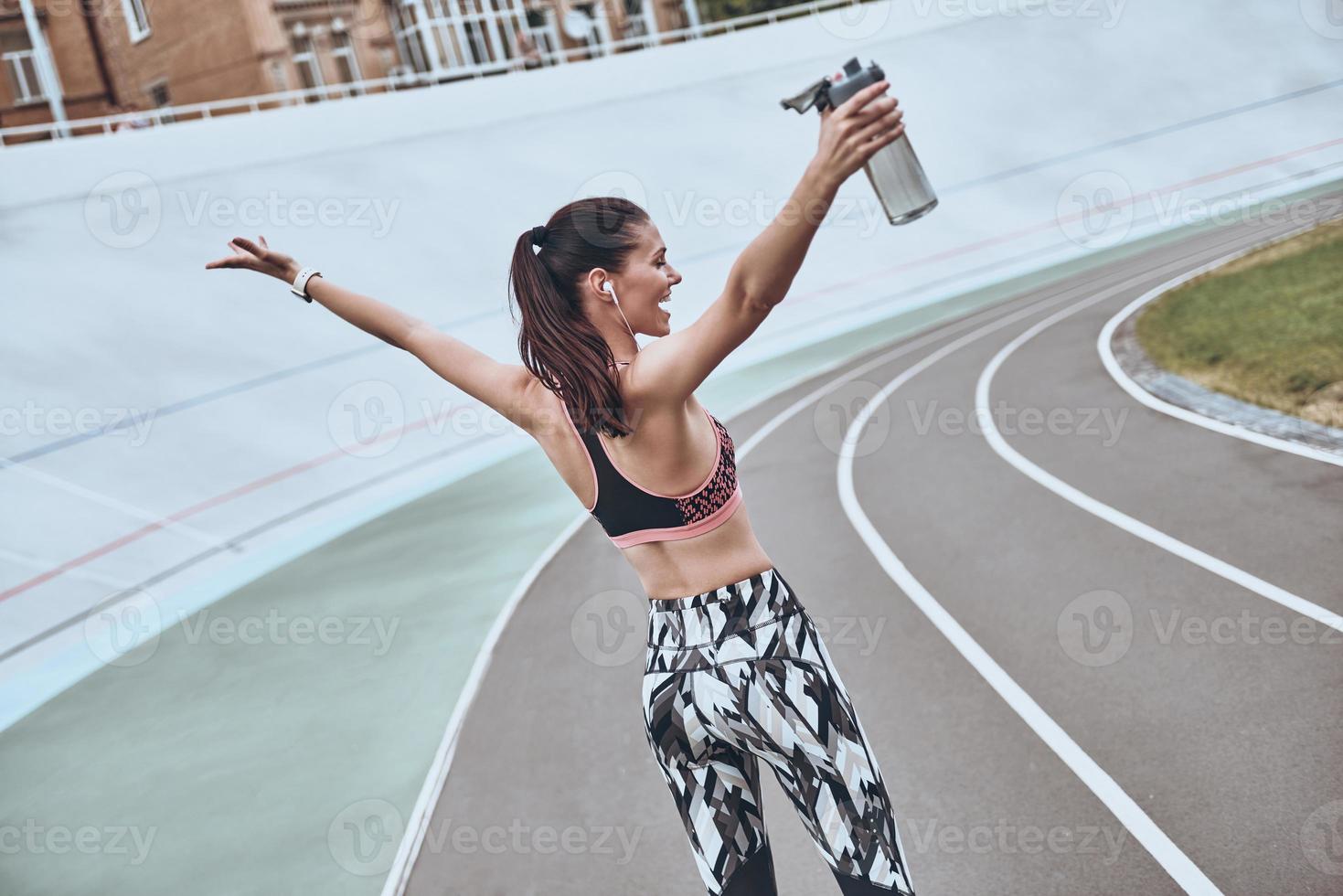 lo hice vista trasera de una mujer joven con ropa deportiva sonriendo y manteniendo los brazos extendidos mientras estaba de pie al aire libre foto