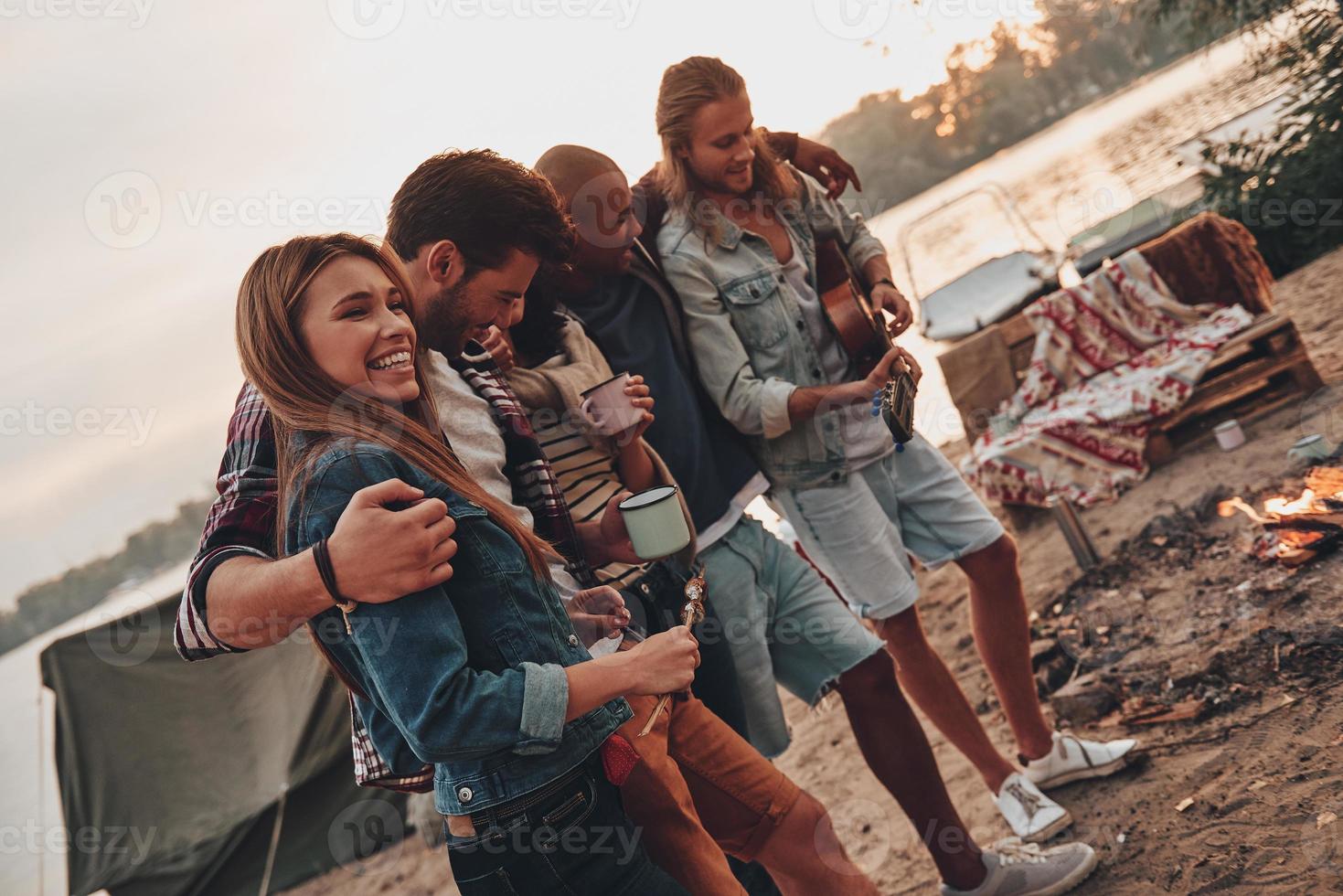 Happy to be around. Group of young people in casual wear smiling and embracing while enjoying beach party near the lake photo