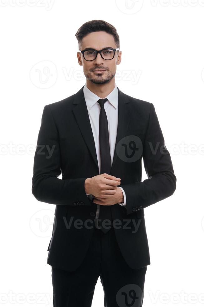 Portrait of style. Handsome young man in full suit adjusting his sleeve and looking at camera with smile while standing against white background photo
