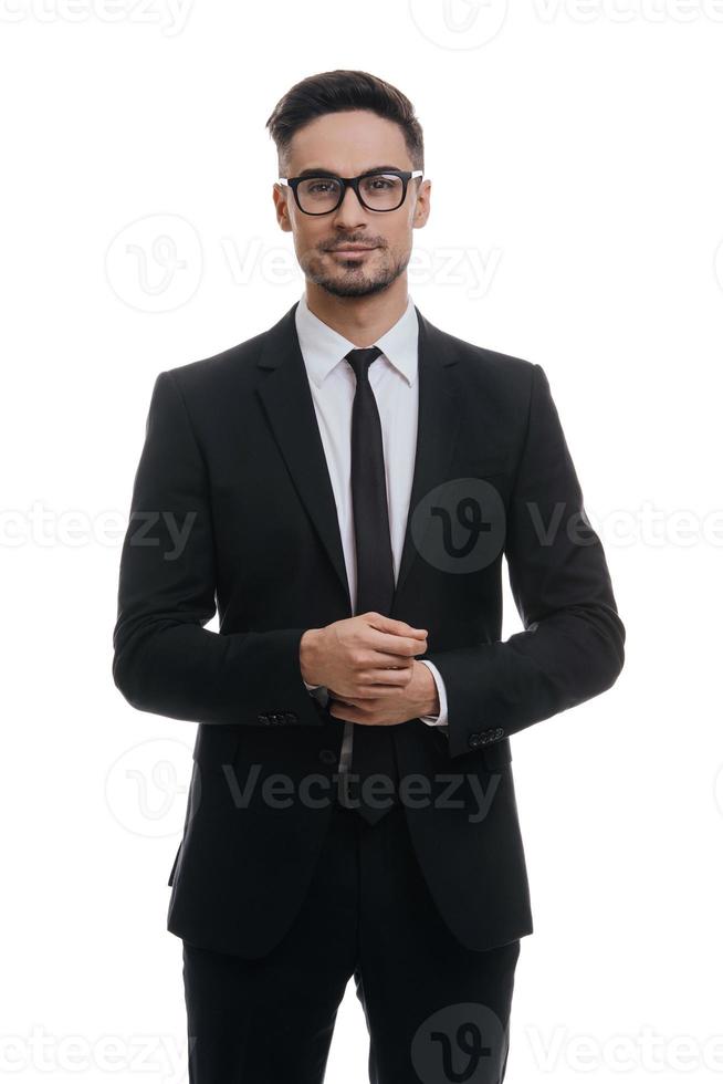 retrato de estilo. un joven apuesto con traje completo ajustándose la manga y mirando a la cámara con una sonrisa mientras se enfrenta a un fondo blanco foto