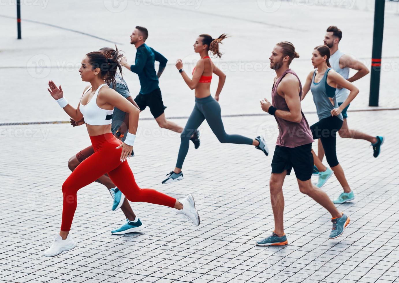 Full length of young people in sports clothing jogging while exercising on the sidewalk outdoors photo