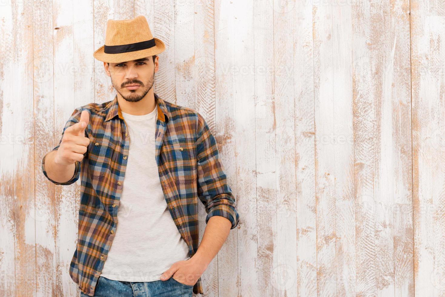 He chooses you. Portrait of handsome young man looking and pointing at camera while standing against the wooden wall photo