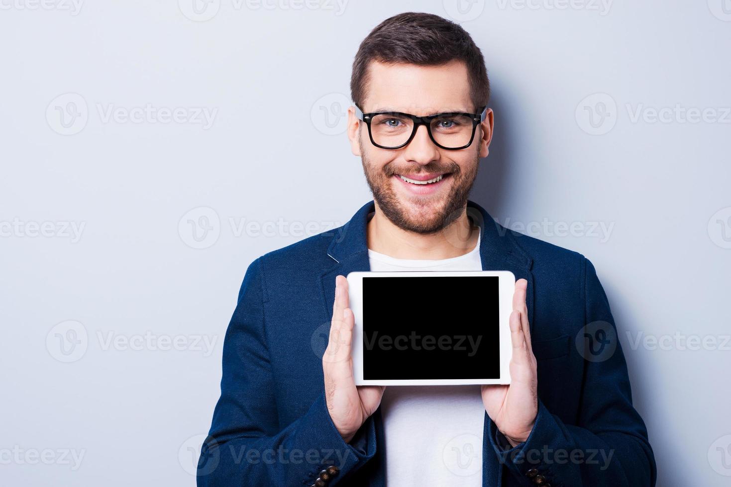 Copy space on his tablet. Cheerful young man holding a digital tablet and smiling while standing against grey background photo