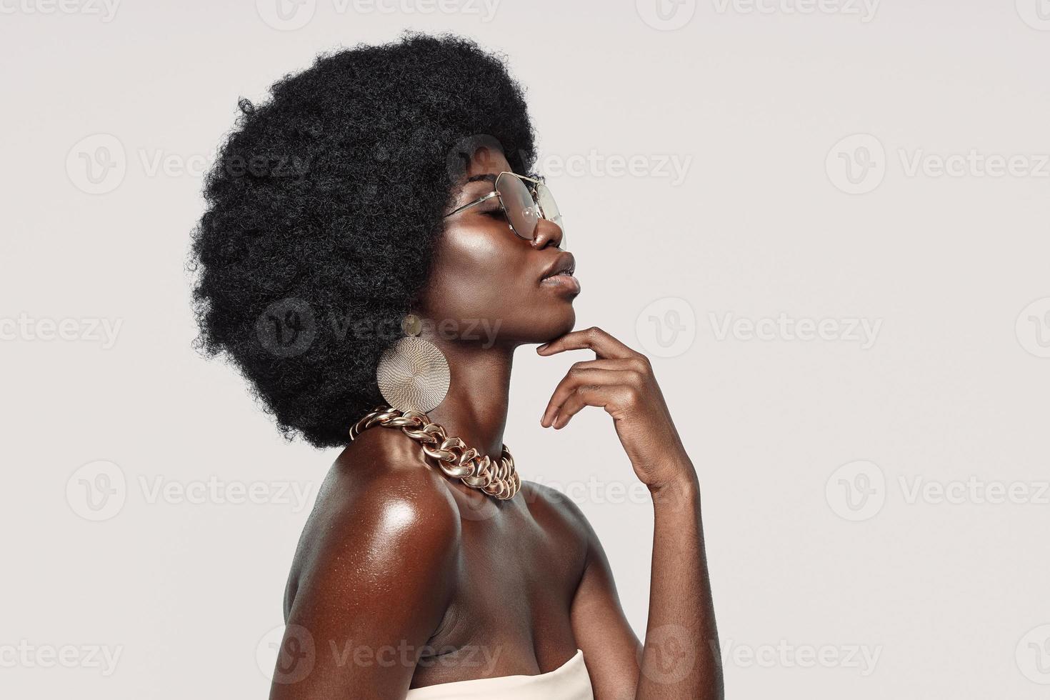 Side view of beautiful young African woman in golden jewelry keeping eyes closed and touching face photo