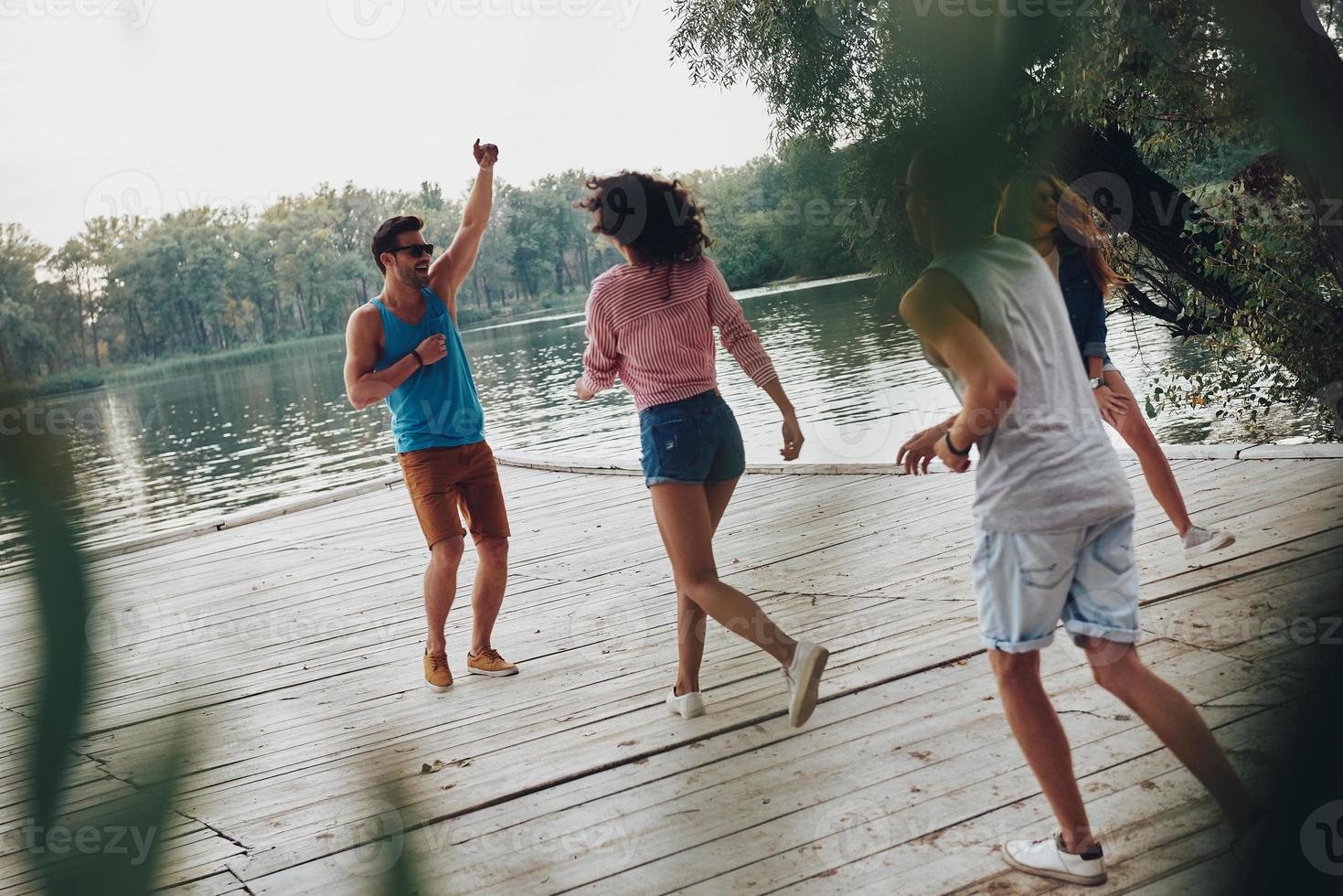 diversión sincera. toda la longitud de los jóvenes en ropa casual sonriendo y divirtiéndose mientras están de pie en el muelle foto