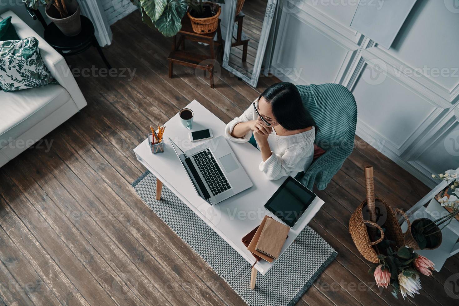 decisión difícil de tomar. vista superior de una hermosa joven que trabaja usando una computadora mientras está sentada en la oficina de su casa foto