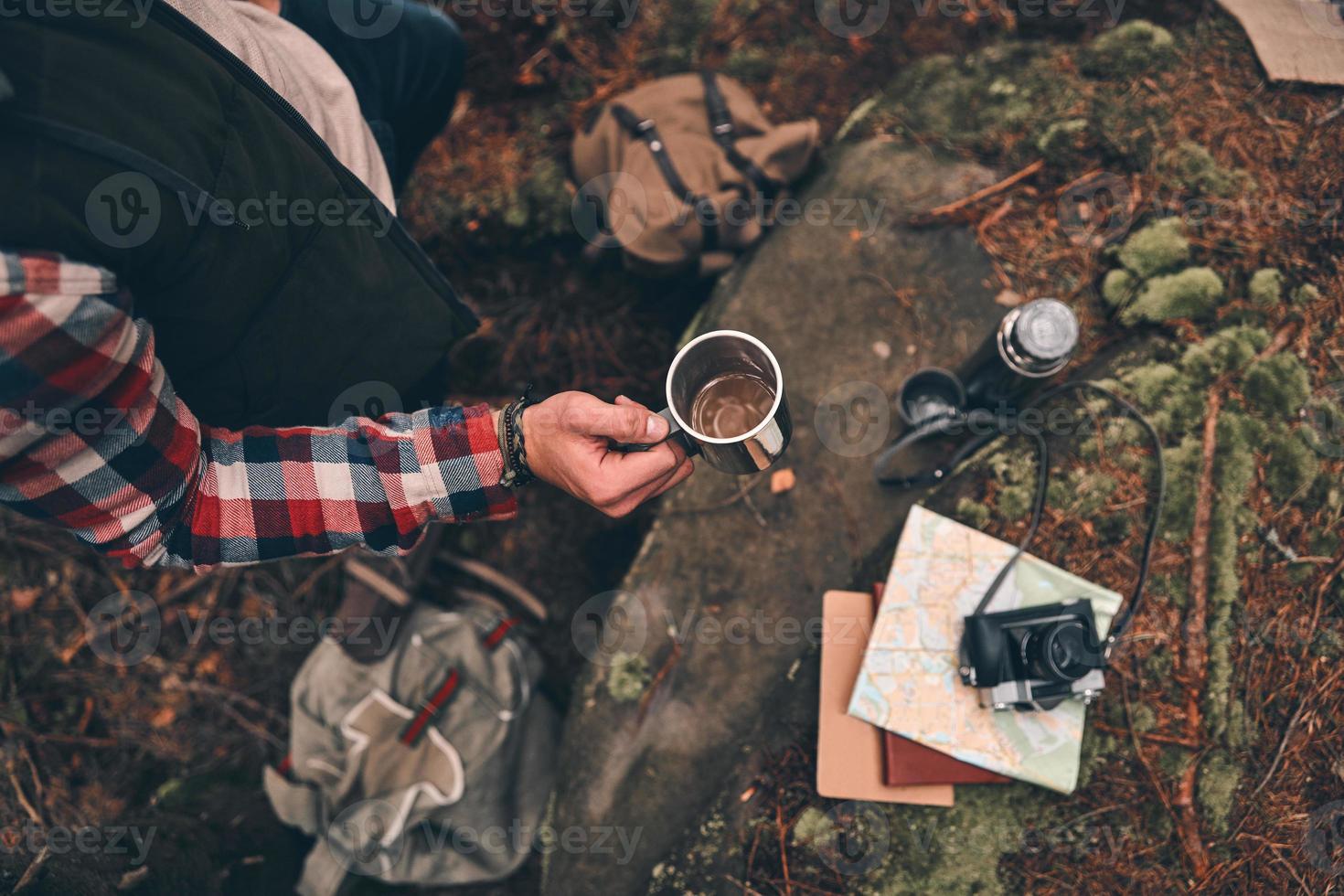 Need another hot drink. Close up top view of young man holding a mug while standing in the forest photo