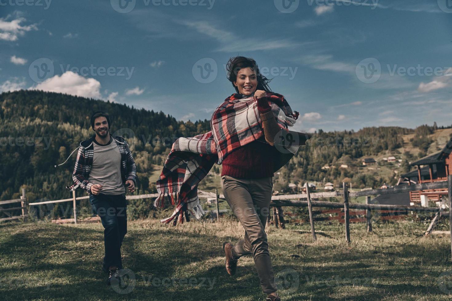 Playful and filled with love. Happy young couple smiling while running on the valley in mountains outdoors photo