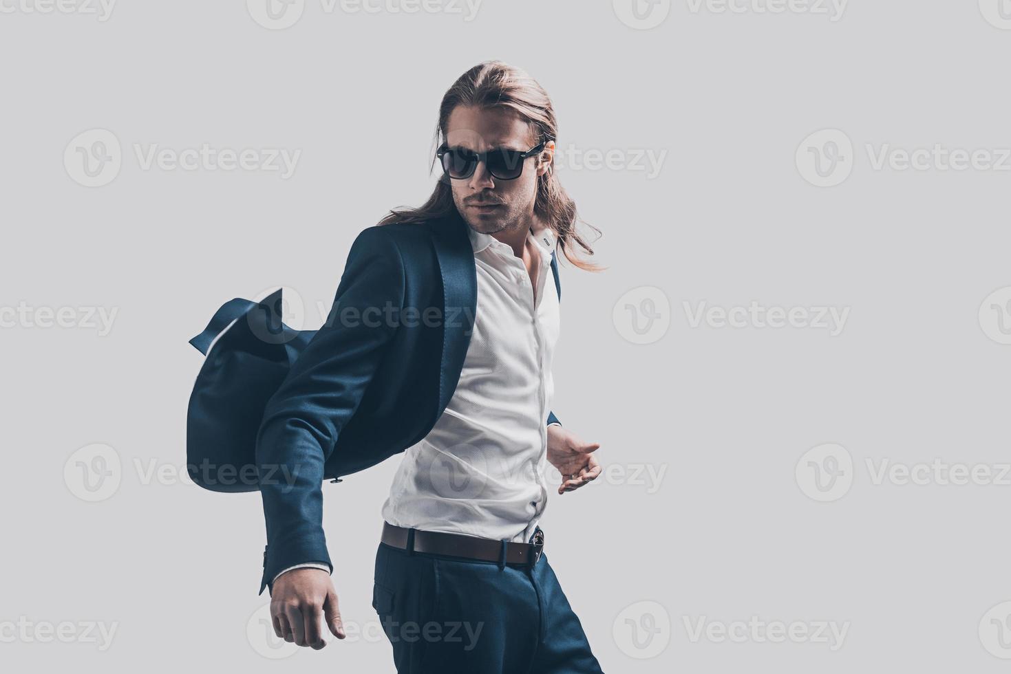 Feeling free and comfortable in his style. Handsome young man in full suit and sunglasses moving in front of grey background photo