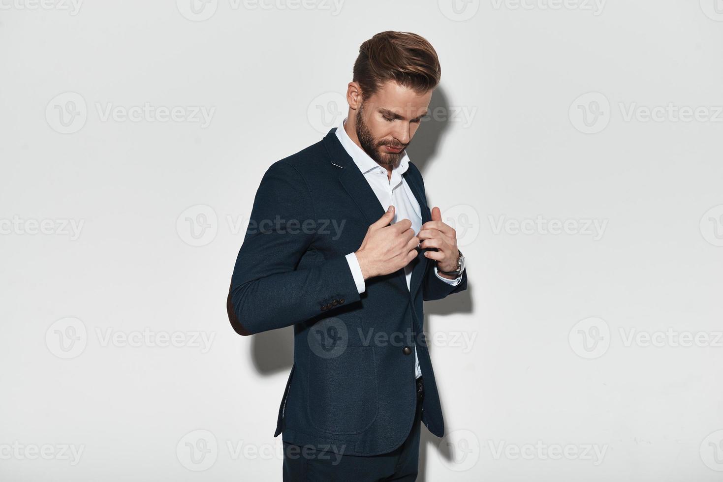 Perfect style. Handsome young man in full suit adjusting his jacket while standing against grey background photo