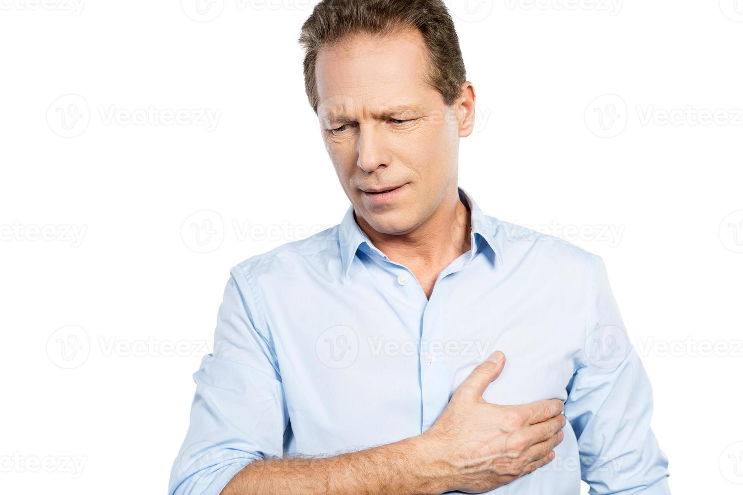 Pain in heart. Frustrated mature man holding hand on heart and expressing negativity while standing against white background photo