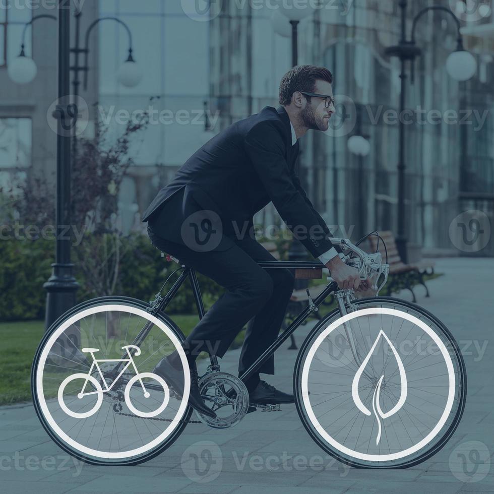 Green ride. Side view of young businessman looking forward while riding on his bicycle photo