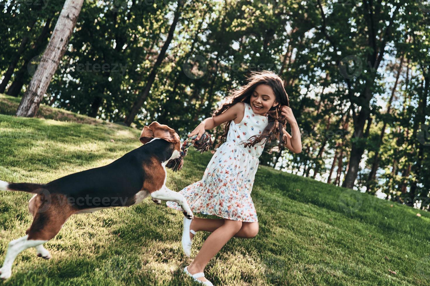 Full length of cute little girl playing with her dog and smiling while running outdoors photo
