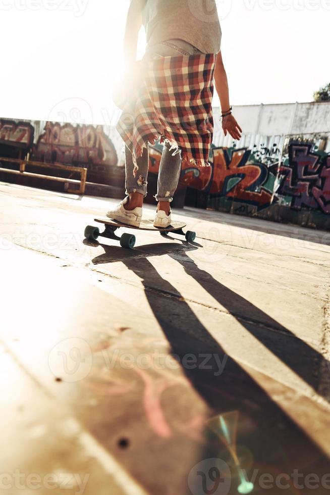 Close-up rear view of modern young man skateboarding while hanging out at the skate park outdoors photo