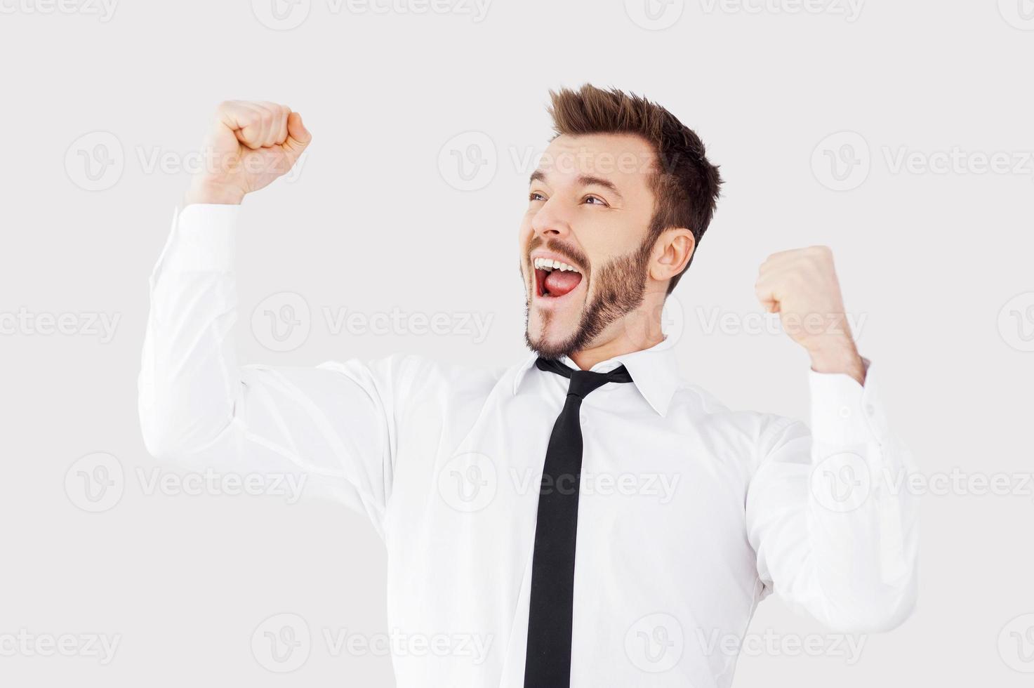 Successful businessman. Happy young man in shirt and tie gesturing while standing against grey background photo