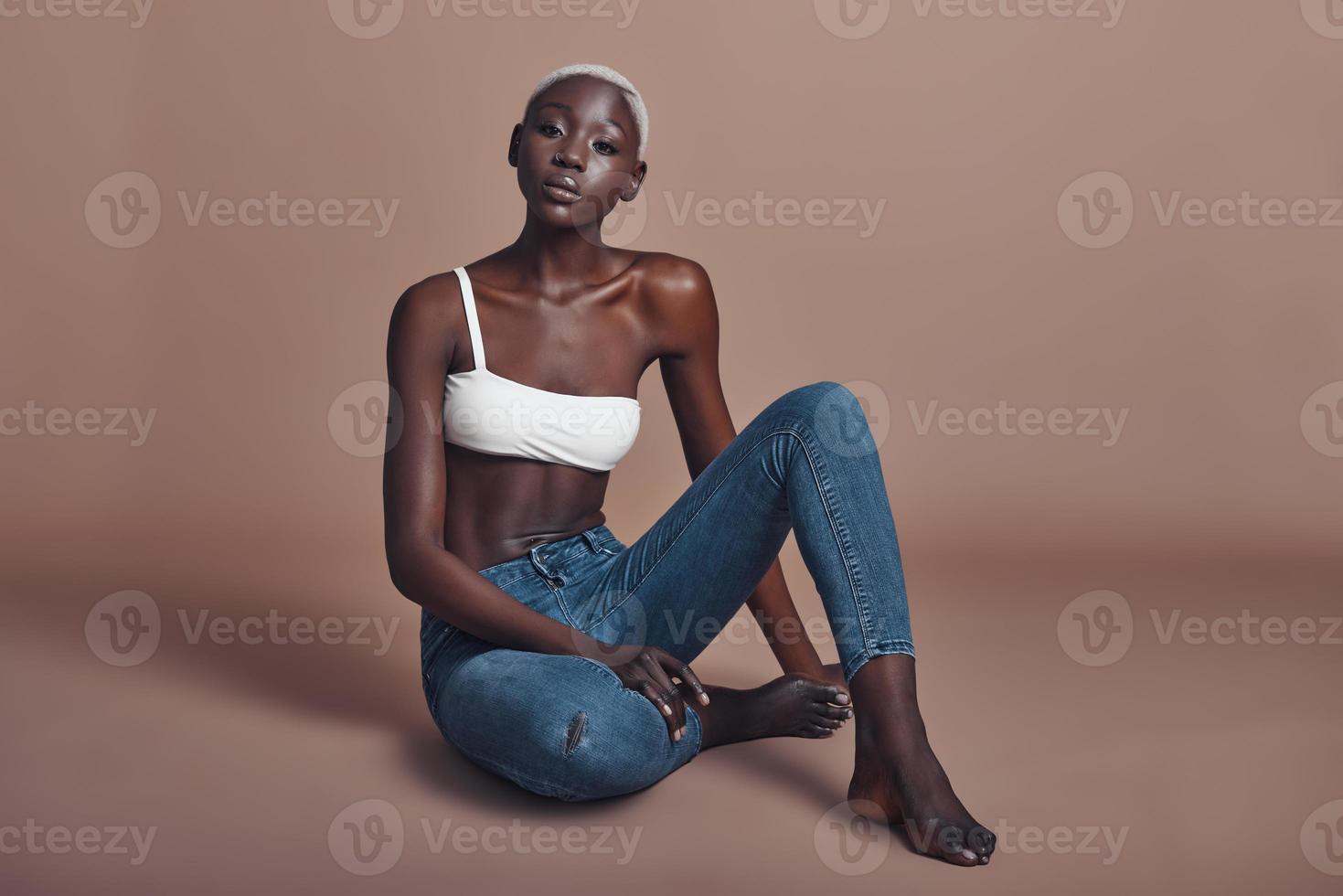 Looking just perfect. Attractive young African woman looking at camera while sitting against brown background photo