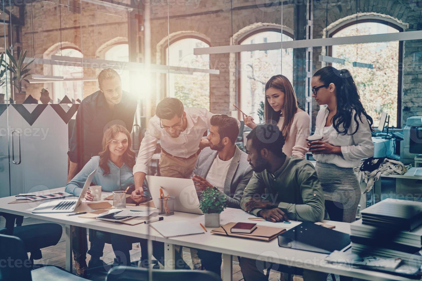 Group of young modern people in smart casual wear communicating and using modern technologies while working in the office photo