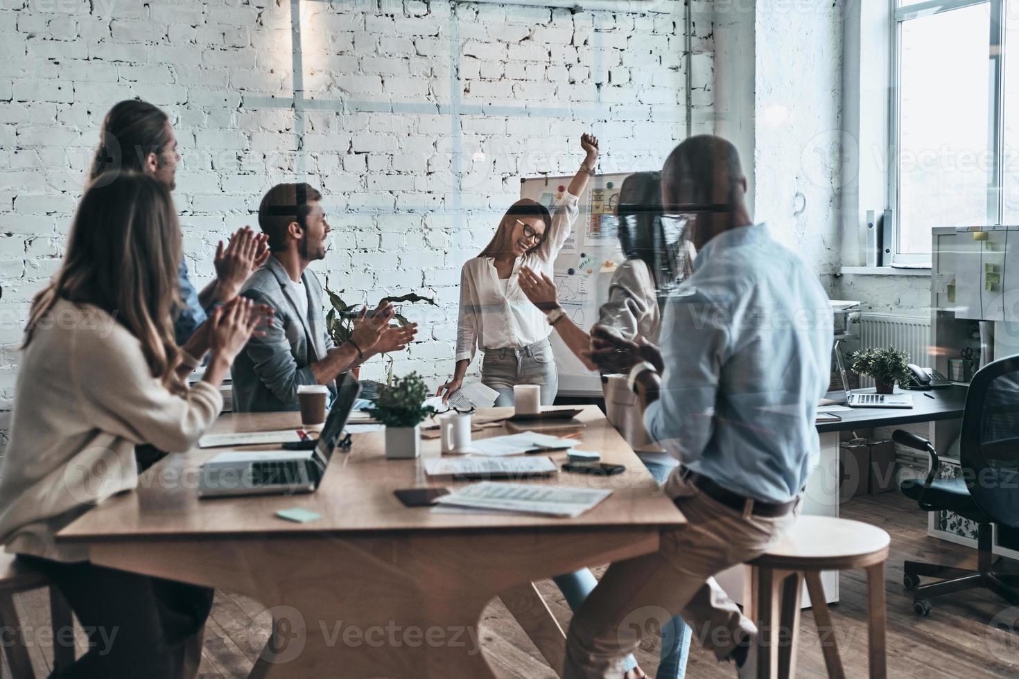 Success achieved. Modern young business people clapping and smiling while working behind the glass wall in the board room photo