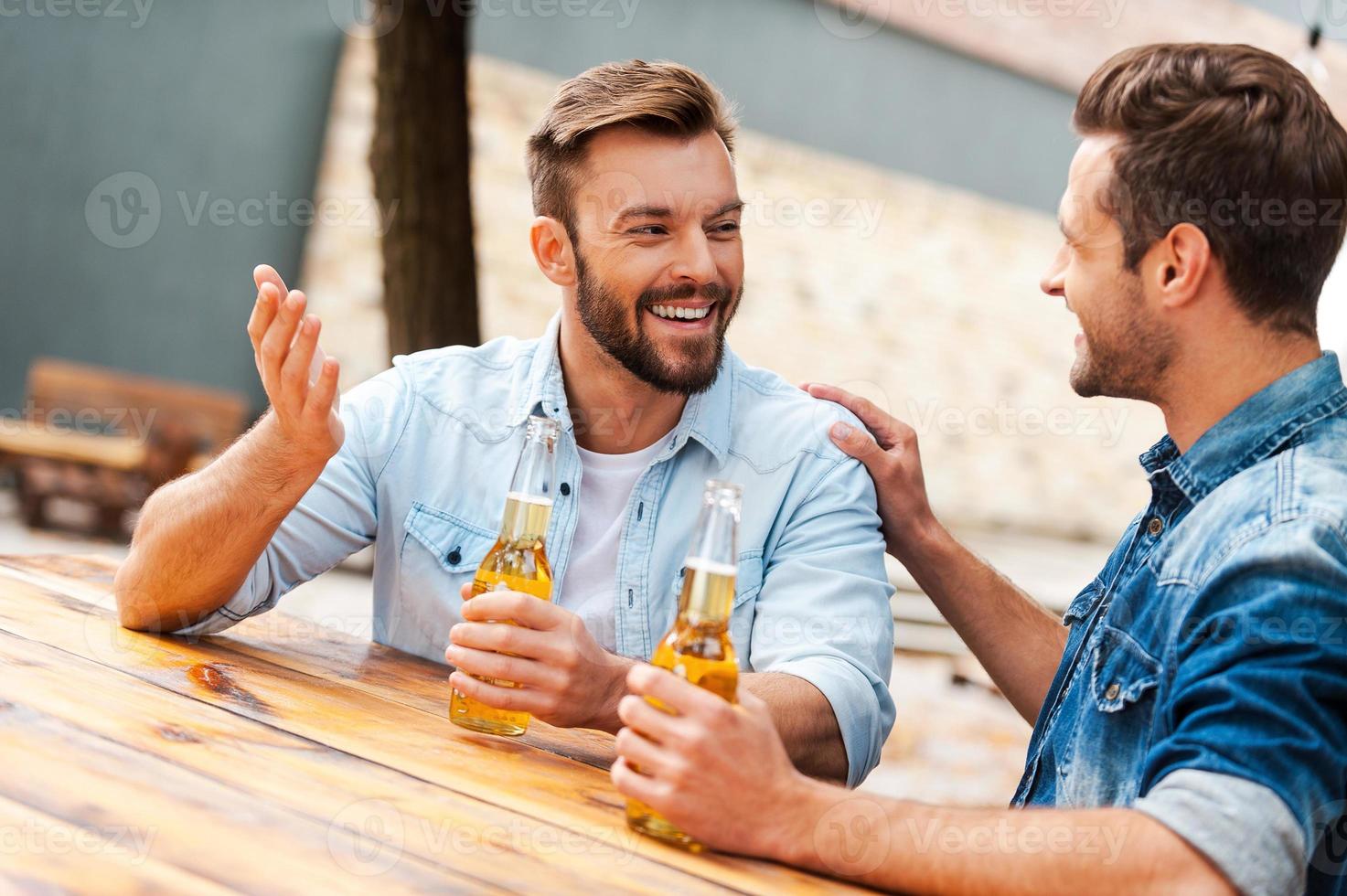 Beer time. Two cheerful young men talking to each other and holding bottles with beer while standing outdoors photo