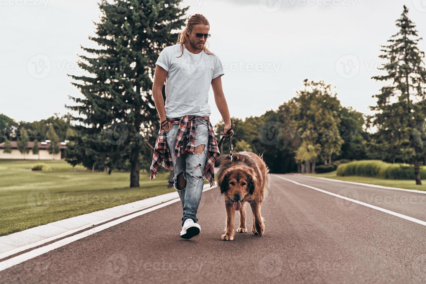 Enjoying good walk. Full length of handsome young man walking with his dog while spending time outdoors photo